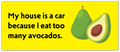 A bright yellow rectangular sign or sticker with black text reading 'My house is a car because I eat too many avocados.' and an illustration of a whole avocado next to a cut avocado showing the pit.