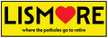 A bright yellow rectangular sign or sticker with a black border. The word 'LISMORE' is printed in large black letters, with a red heart replacing the 'O'.