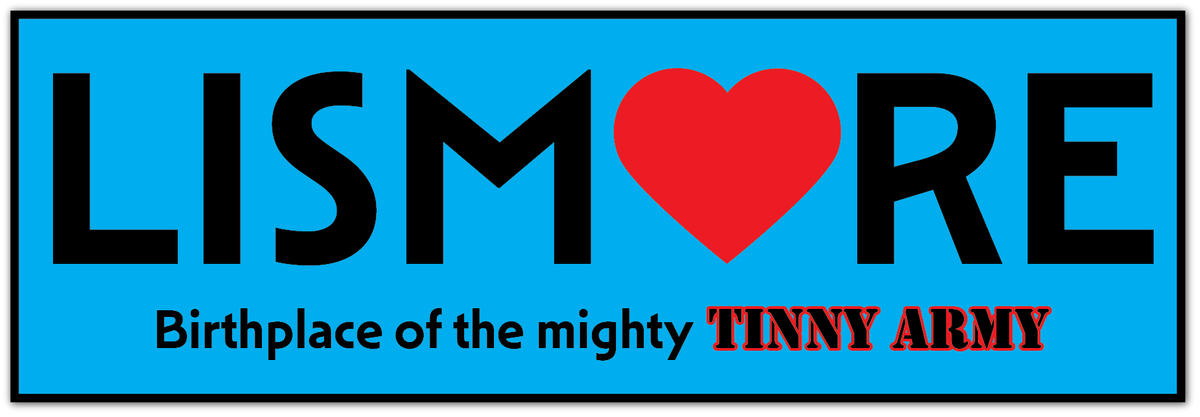 A square graphic with a bright blue background and a black border. Large black text reads 'LISMORE' across the center, with a red heart replacing the O 